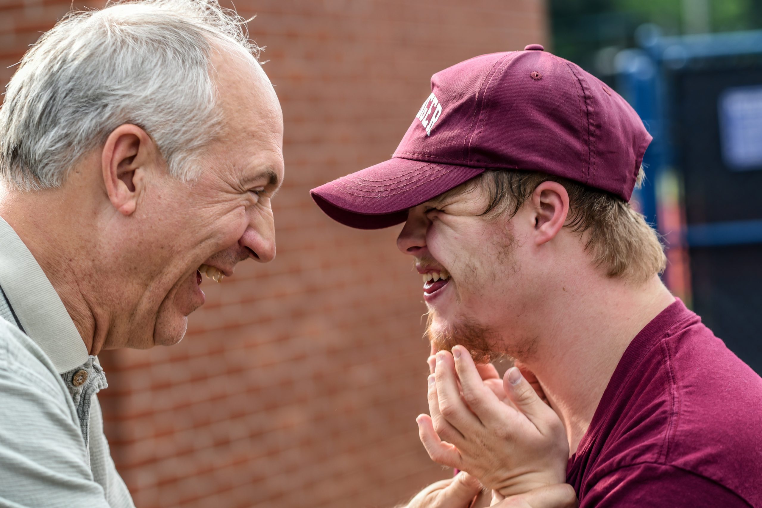 An elderly man and a boy with Down syndrome laughing together in the community garden, enjoying their time surrounded by greenery.